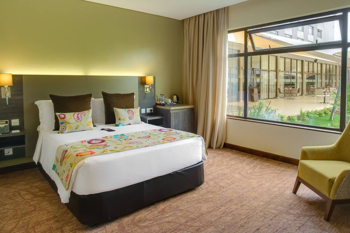 A hotel room with a large bed, a chair, a desk, and a view of the outdoor area.