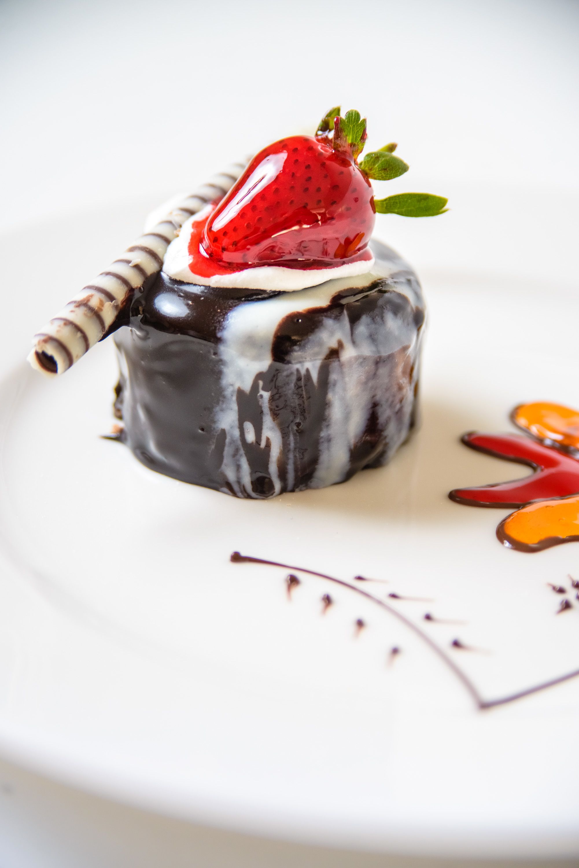 A dessert with a chocolate-covered cake, a strawberry on top, and a dollop of cream.