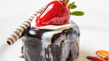 A dessert with a chocolate-covered cake, a strawberry on top, and a dollop of cream.