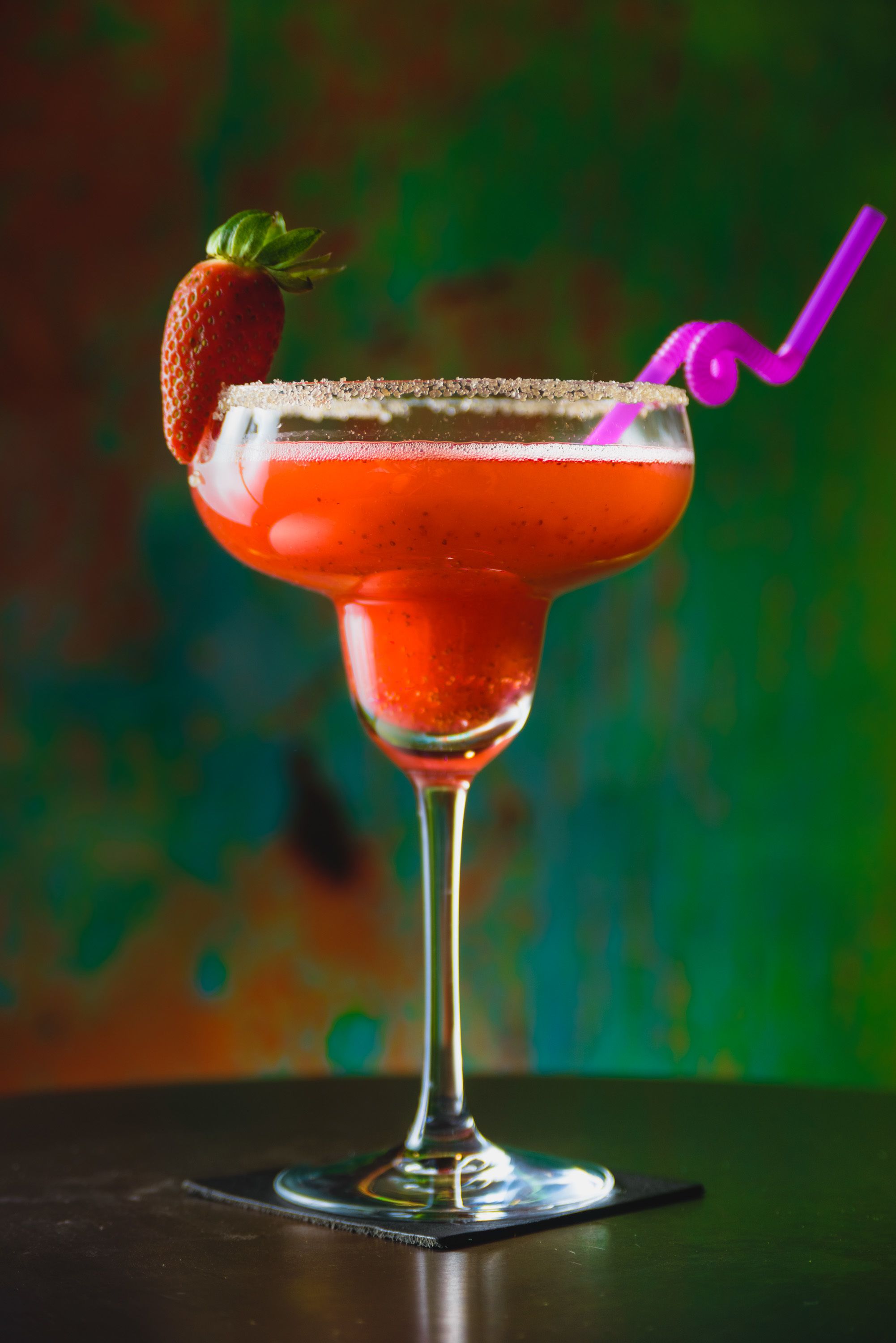 Ein Cocktail mit Erdbeerdekor und einem violetten Strohhalm in einem Glas mit Salzrand.