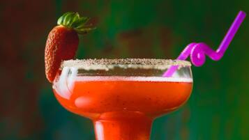 Ein Cocktail mit Erdbeerdekor und einem violetten Strohhalm in einem Glas mit Salzrand.