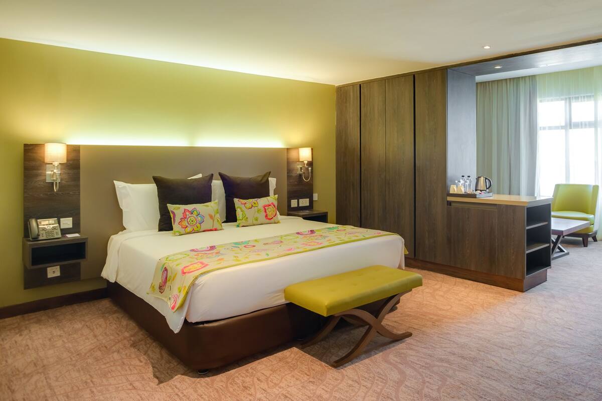 A hotel room with a large bed, bedside tables, a desk, a chair, and a window with curtains.