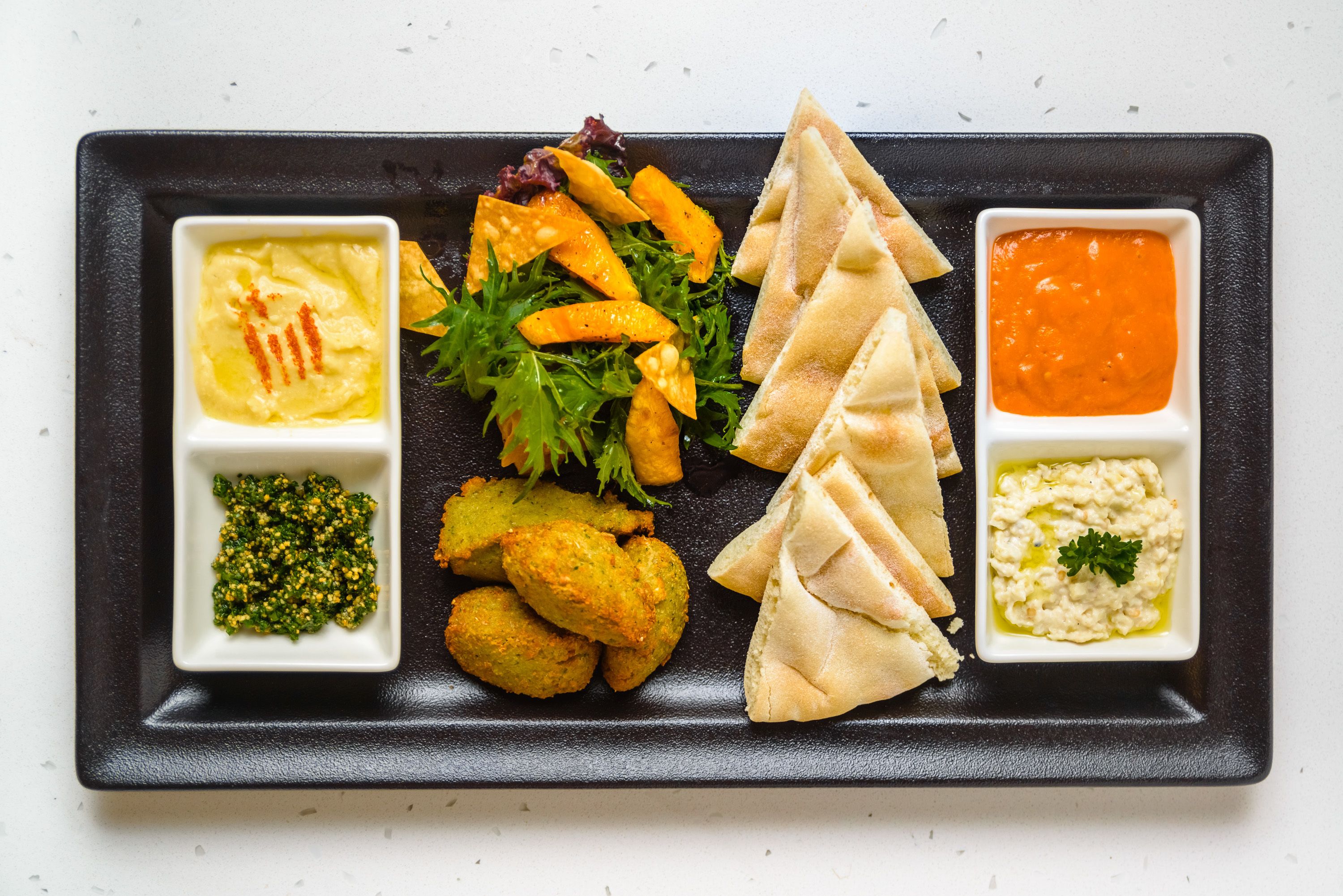 Una bandeja negra rectangular con diversos alimentos, como hummus, falafel, pan de pita y ensalada.