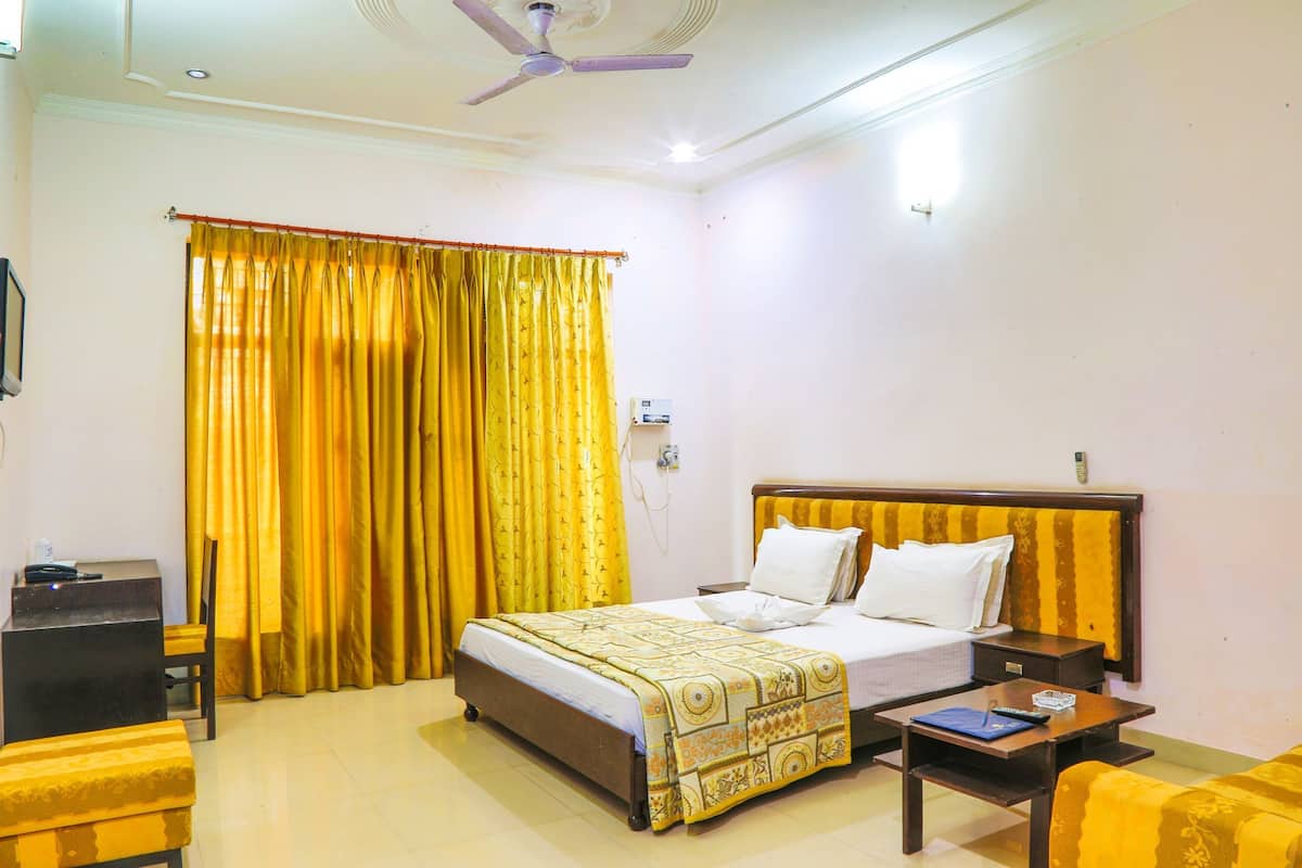 Quarto de hotel com cama, mesa de cabeceira, cadeira e escrivaninha com computador.