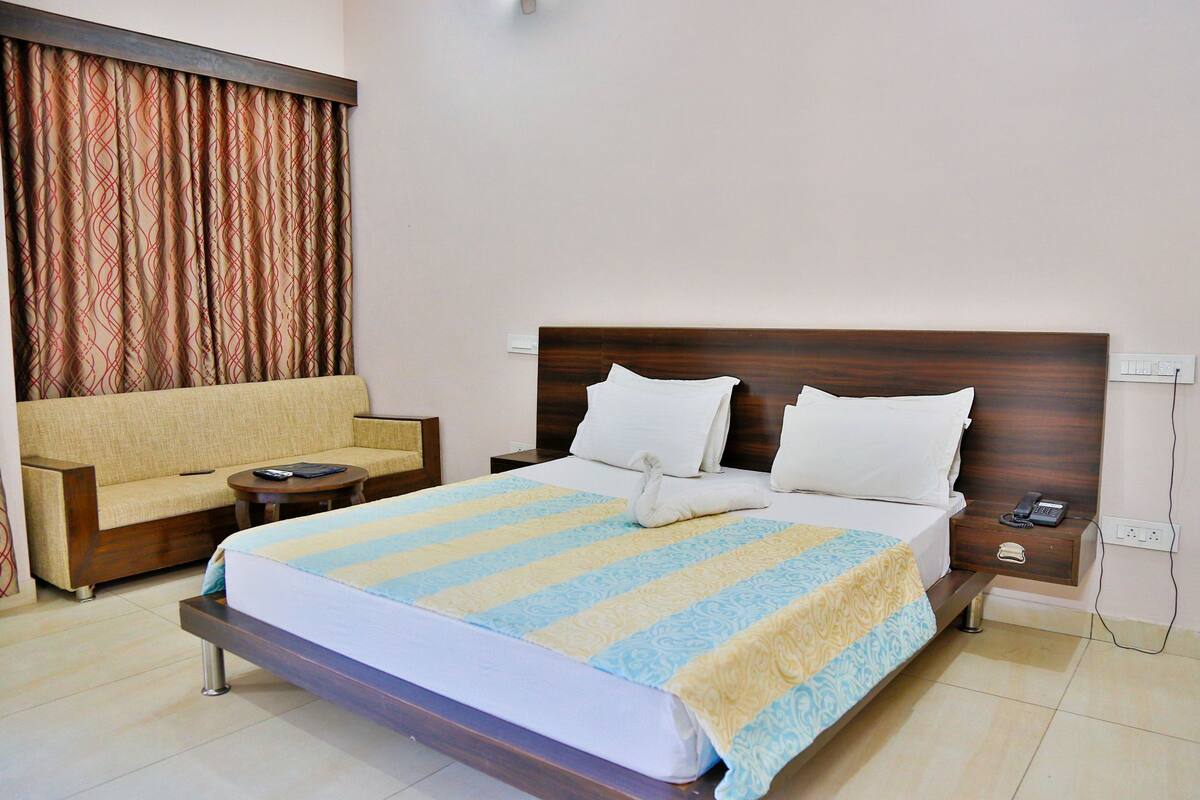 Quarto de hotel com cama, sofá, mesa de cabeceira e criado-mudo.