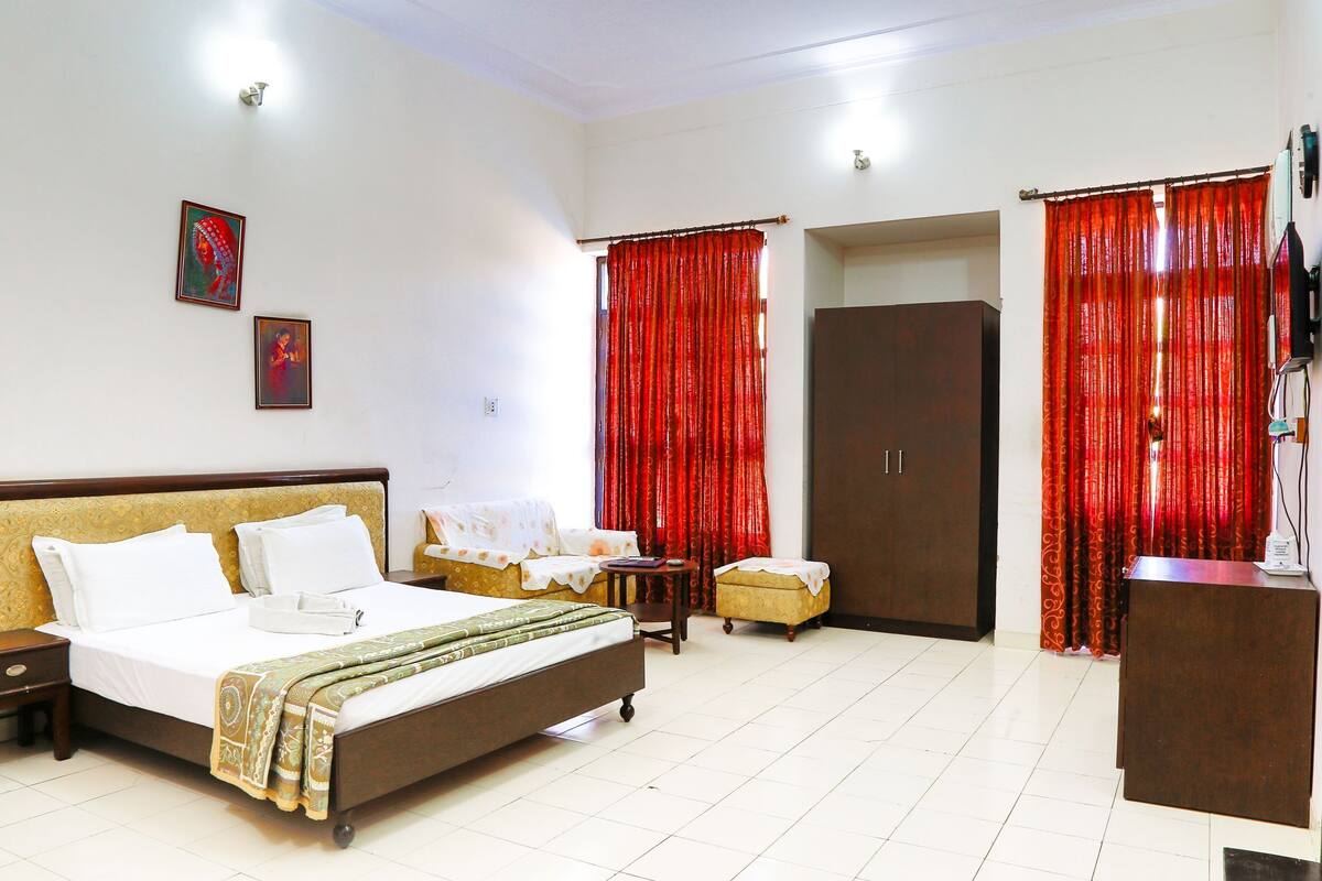 Quarto de hotel com cama, escrivaninha, guarda-roupa e cortinas vermelhas.