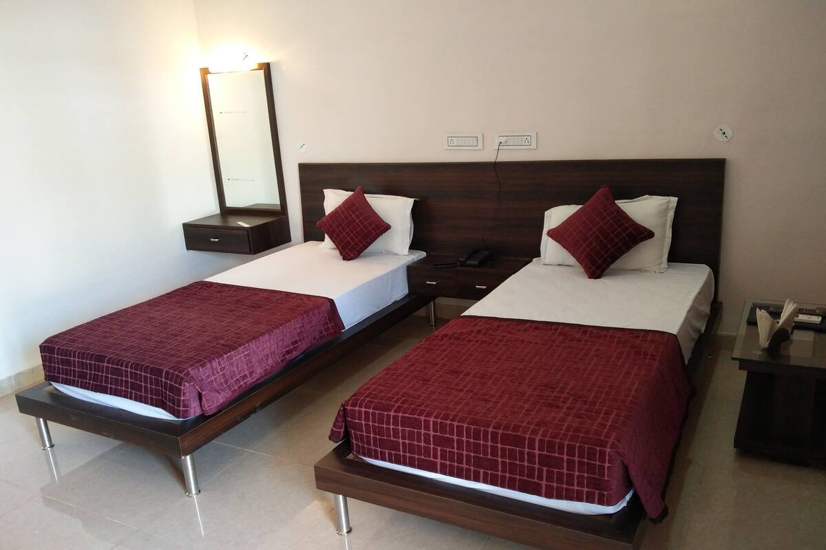 Duas camas de solteiro com roupa de cama vermelha, uma mesa de cabeceira, um espelho e uma tomada na parede.