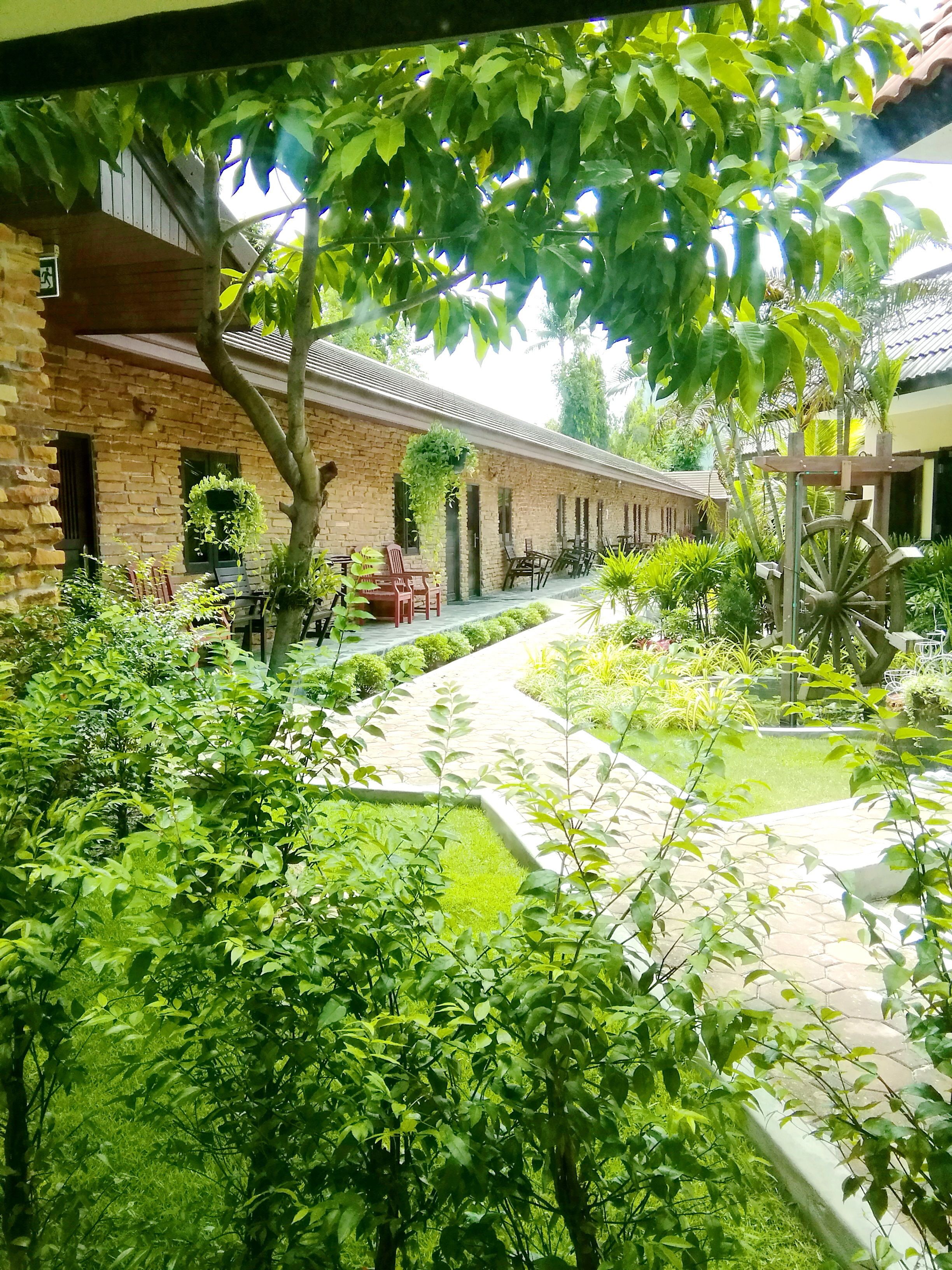 Un patio con un edificio de ladrillo, asientos al aire libre y abundante vegetación.
