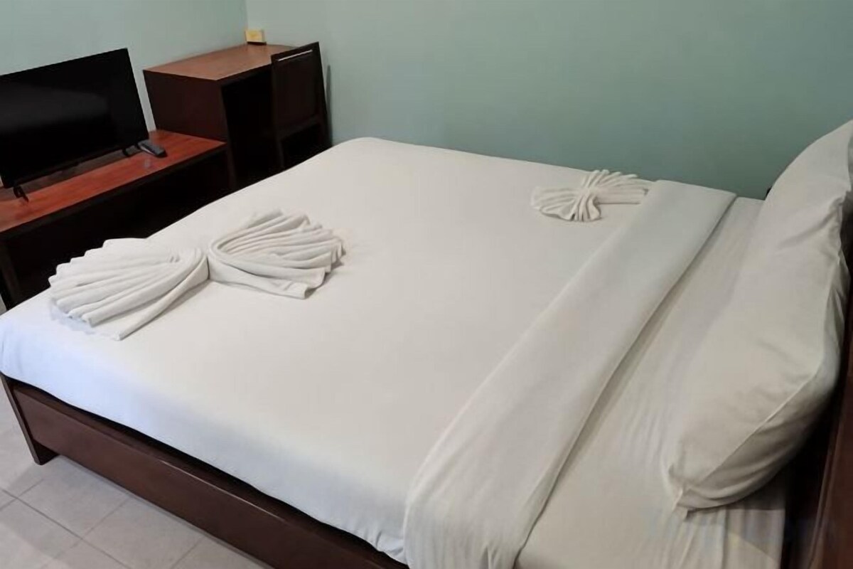 A neatly made bed with towels, a television on a wooden stand, and a plain wall.