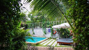A swimming pool surrounded by lush greenery, a lifebuoy, and a bench. - Capricorn Village (Patong)