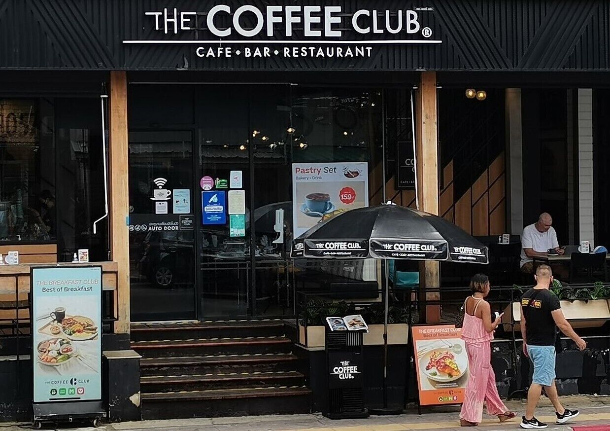 The exterior of The Coffee Club, a cafe, bar, and restaurant with a pastry set sign, outdoor seating, and a staircase leading to the entrance.
