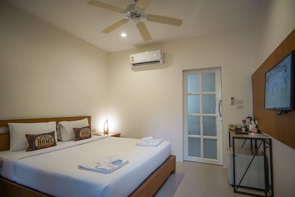 A hotel room with a bed, a ceiling fan, an air conditioning unit, a door, and a small table with a TV.