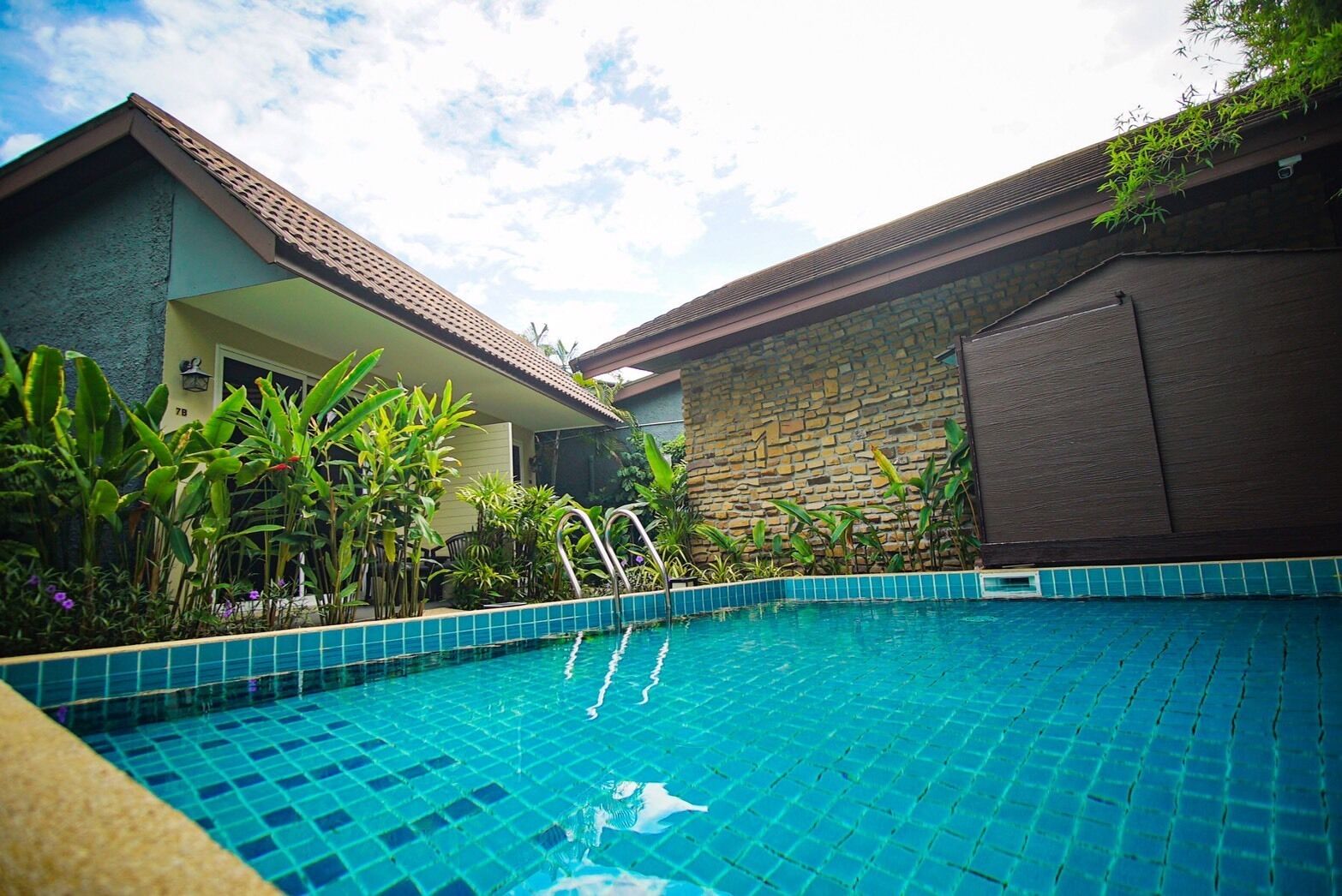 A swimming pool with a tiled edge, surrounded by lush greenery and a stone wall.