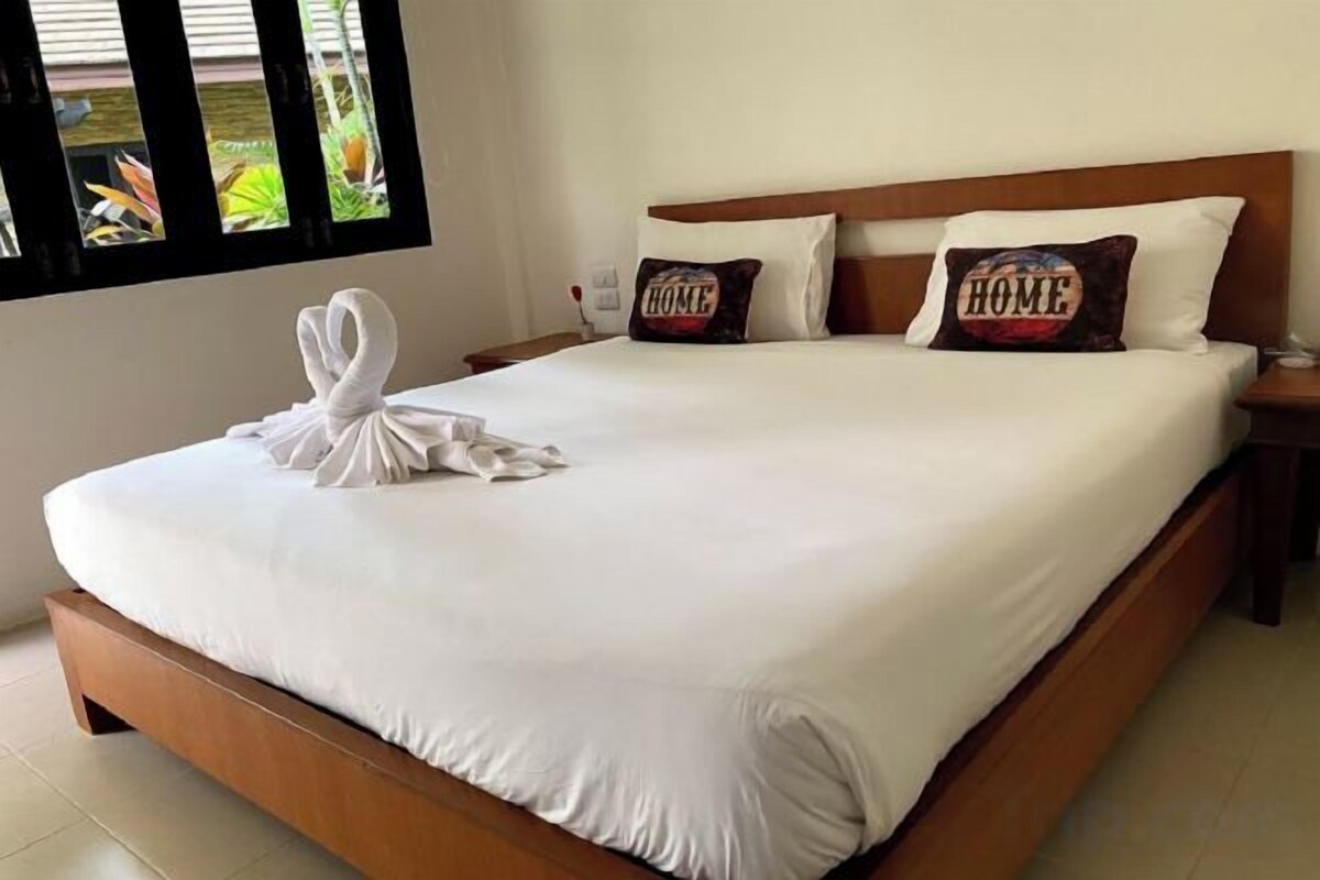 A neatly made bed with a towel arrangement, two pillows with 'HOME' text, and a wooden headboard.