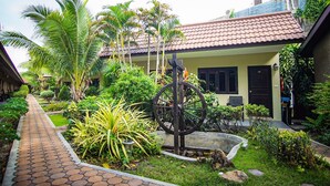 A courtyard with a pathway, palm trees, and a building with a tiled roof. - Capricorn Village (Patong)