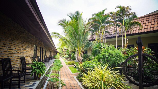 A courtyard with a brick wall, outdoor seating, a paved walkway, and tropical plants. - Capricorn Village (Patong)