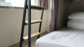 A bunk bed with a ladder, a window with curtains, and a bed with white bedding.