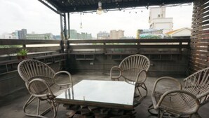 Terraço no telhado com cadeiras de vime e uma mesa de vidro, com vista para a paisagem urbana.