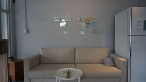 Uma sala de estar moderna com um sofá bege, uma pequena mesa branca com uma planta e uma geladeira.