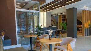 Un interior moderno con mesas y sillas redondas, una recepción y vistas a través de un muro de cristal.