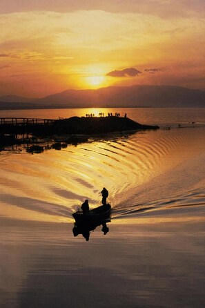 Un atardecer sobre aguas tranquilas, con un muelle y siluetas de personas contra el cielo.