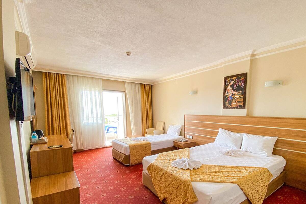 A hotel room with two beds, a wooden headboard, a red carpet, a desk with a chair, and a window with curtains.
