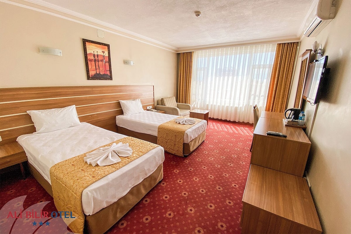 A hotel room with two beds, a desk, a chair, a TV, and a painting on the wall.