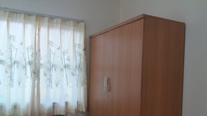 A room with a wooden wardrobe, a small table, and a window with sheer curtains. - 7 Up Resort (Nakhon Nayok)