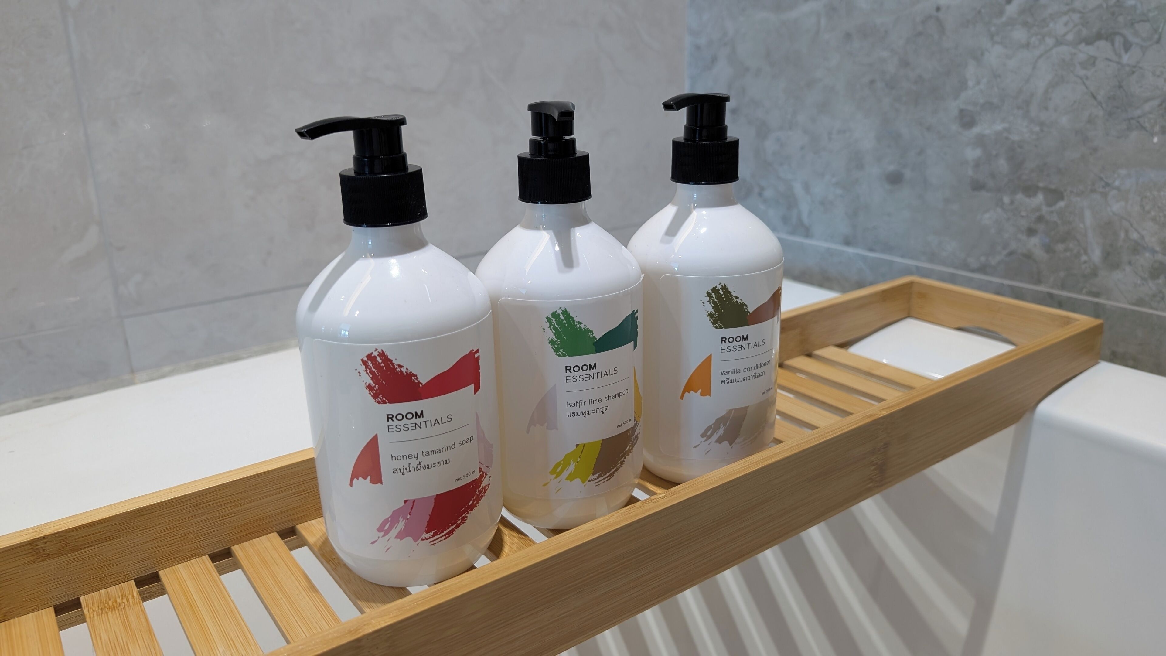 Three bottles of room essentials on a wooden tray in a bathroom.