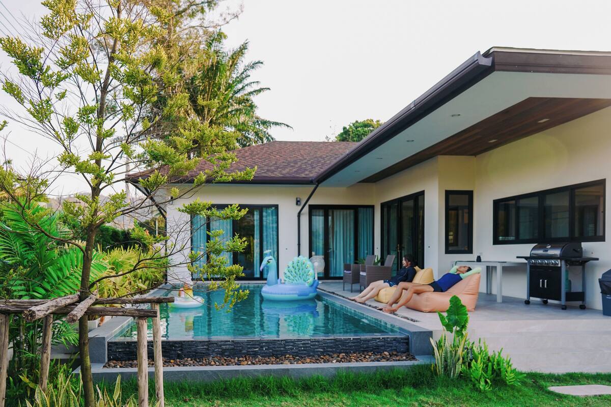 Una casa moderna con piscina, mobiliario de exterior y zona de barbacoa.