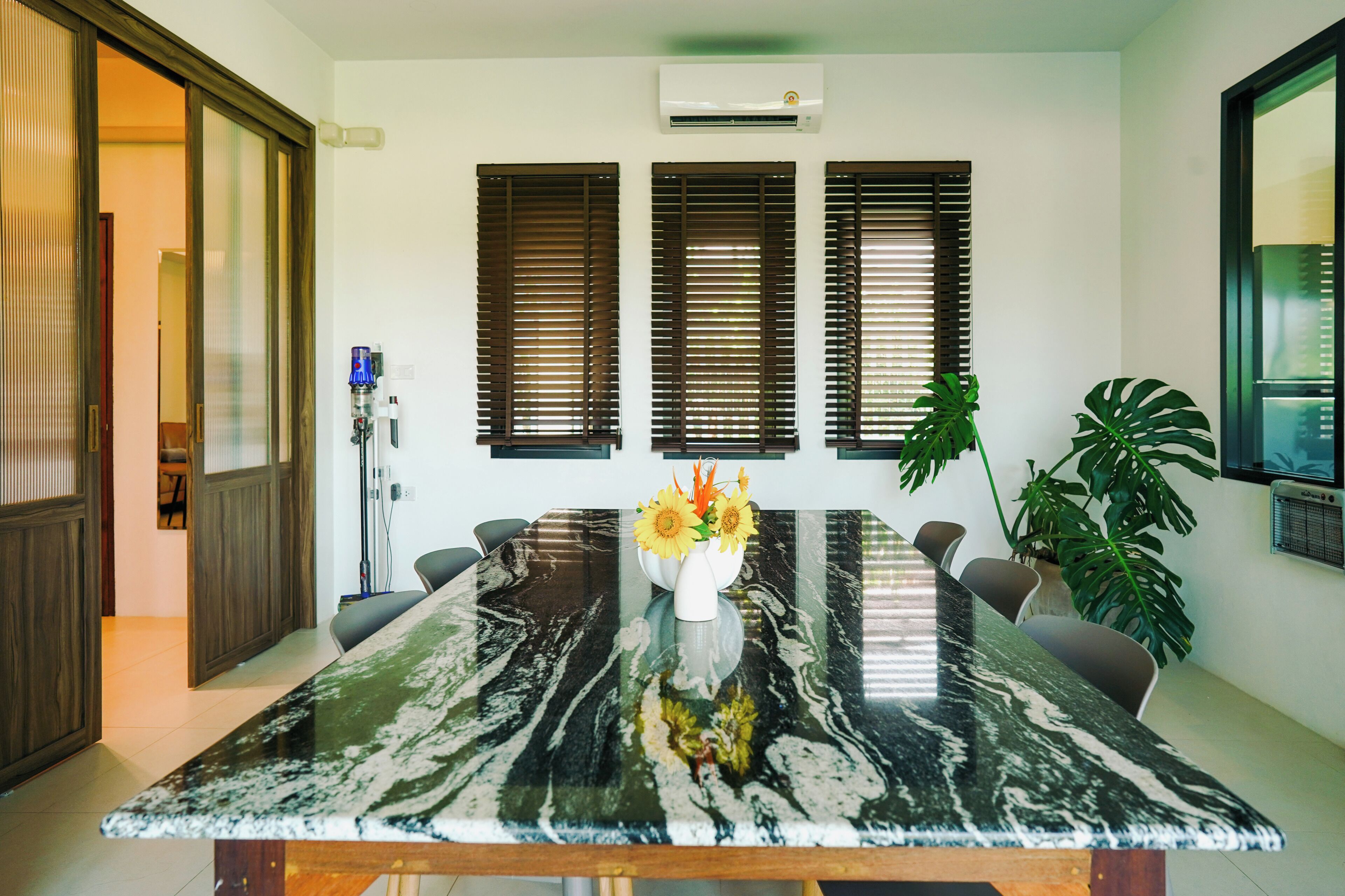Un comedor con mesa de mármol, persianas de madera y una planta en maceta.