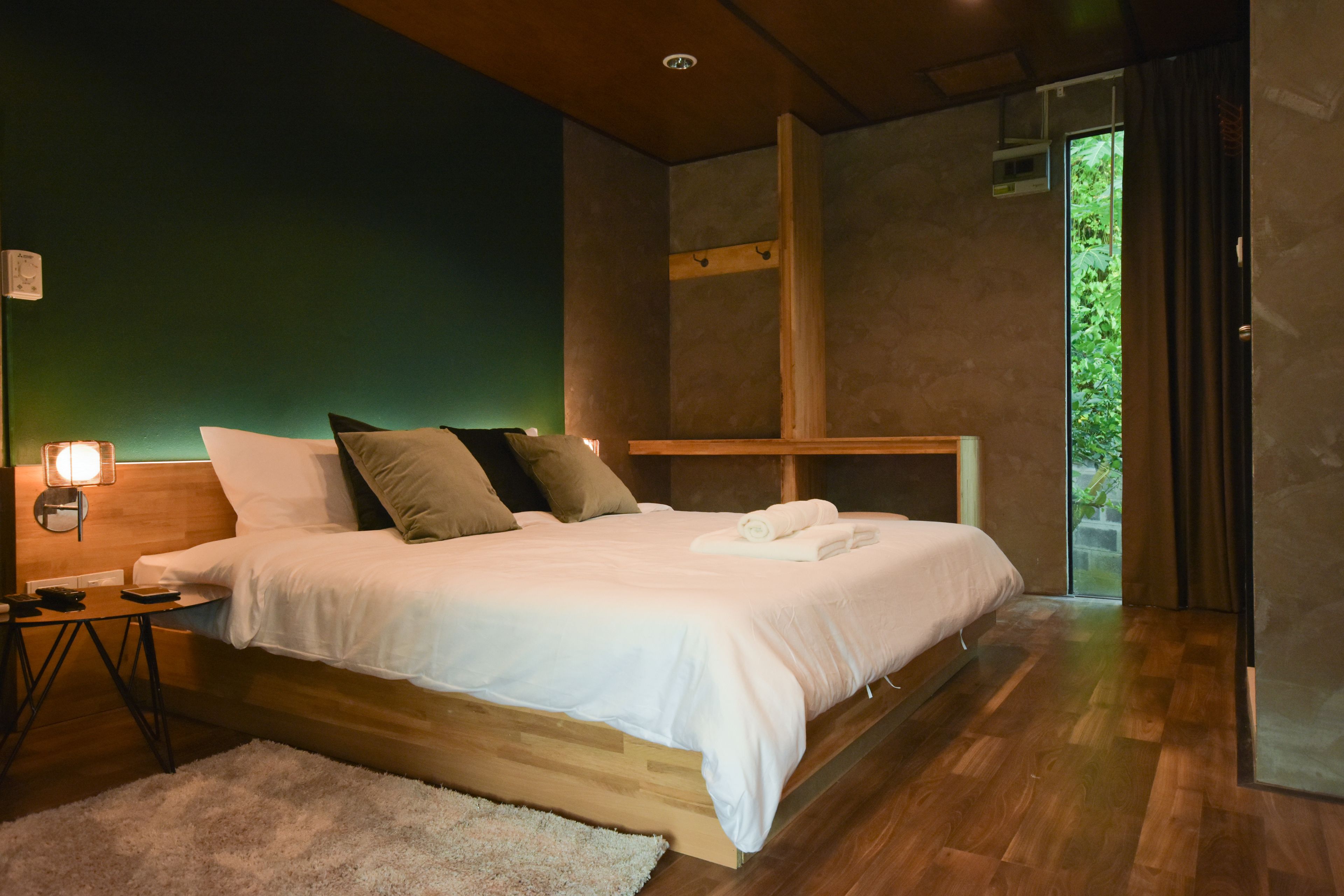 Un dormitorio moderno con una cama de madera, una mesita de noche y un amplio ventanal con vistas a la vegetación.