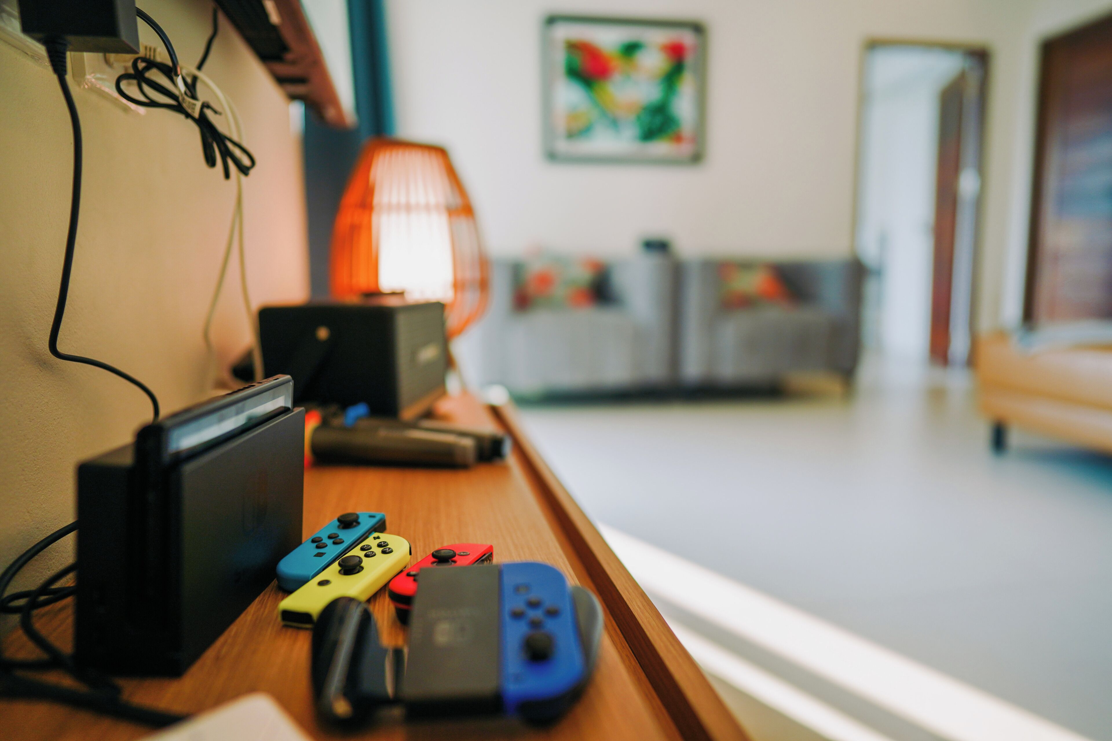 A wooden table with a Nintendo Switch, various game controllers, and a lamp.