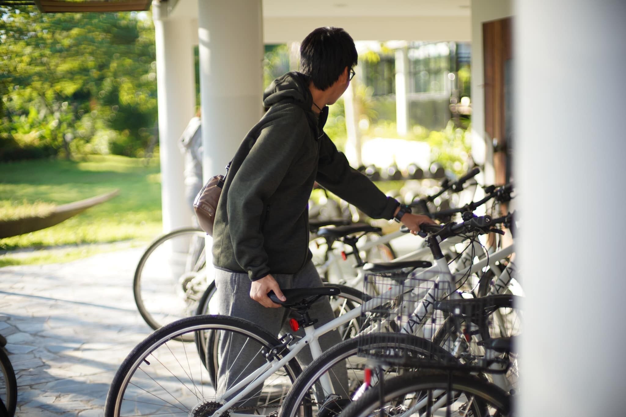 A person leaning on a bicycle in a covered outdoor area with multiple bicycles parked nearby.