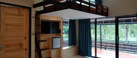 A modern room with a loft bed, built-in TV, and large windows offering a view of the outdoors.