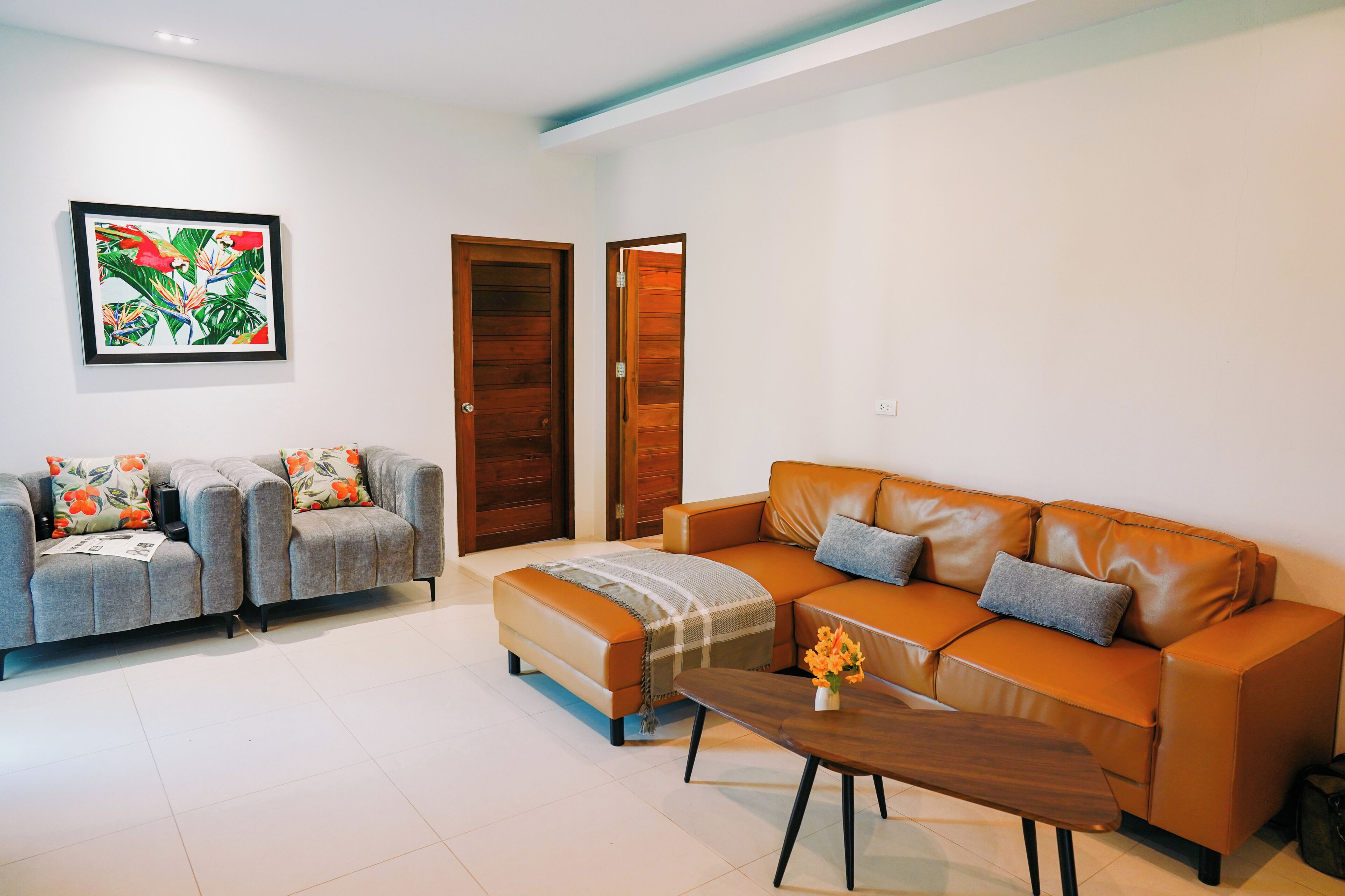 A living room with a grey sofa, an orange sofa, a coffee table, and a painting on the wall.