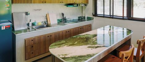 A kitchen with wooden cabinets, a built-in island, a refrigerator, and a window with blinds.