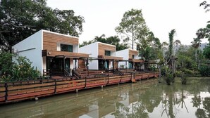 Een modern gebouw met een houten gevel, gelegen aan een rustig waterlichaam, omgeven door weelderige begroeiing.