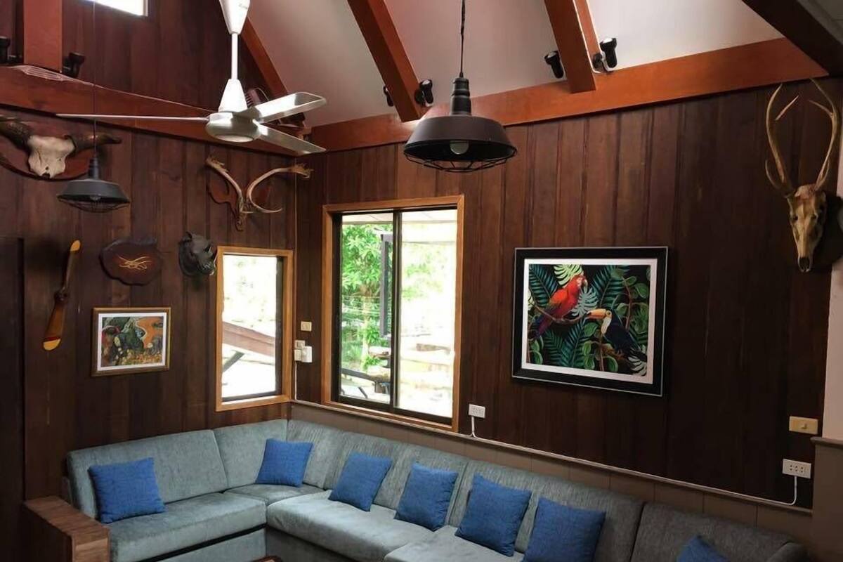 Una sala moderna con un sofá seccional gris, paredes de madera y un ventanal grande.