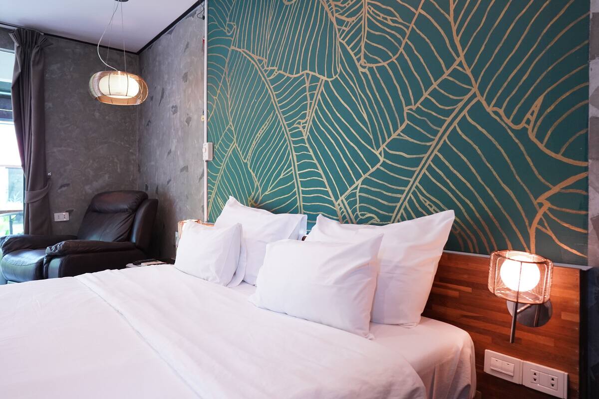 Una habitación de hotel con una cama grande, una silla y una pared con un diseño de hojas.