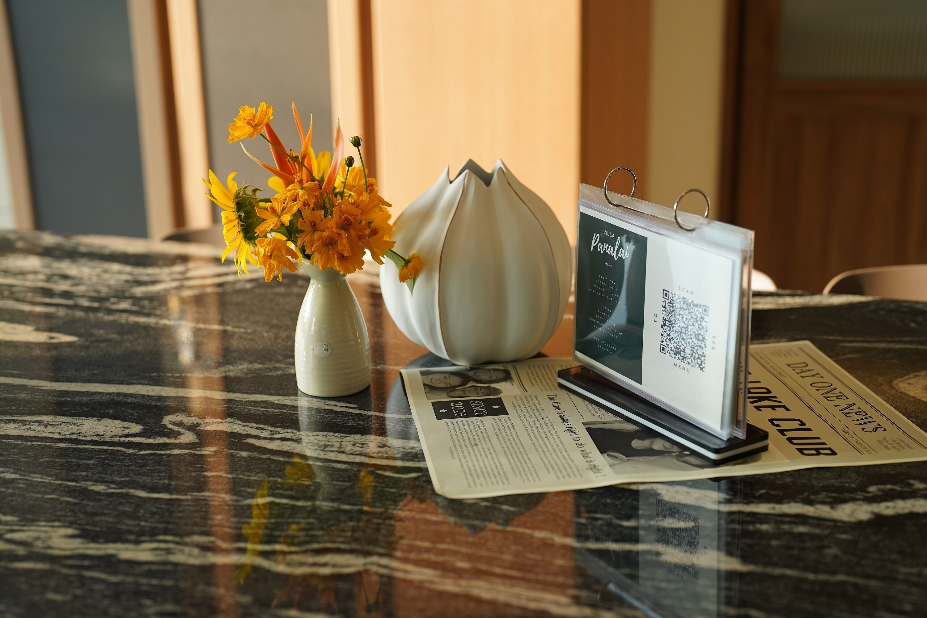 A table with a vase of flowers, a modern tablet, and a newspaper.