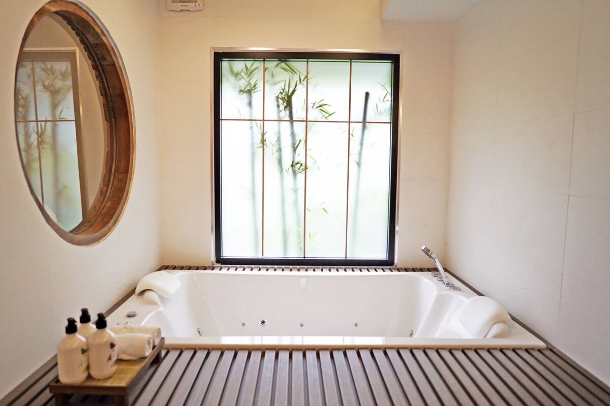 Un baño moderno con una bañera independiente, un tocador de madera con artículos de aseo y un espejo grande.