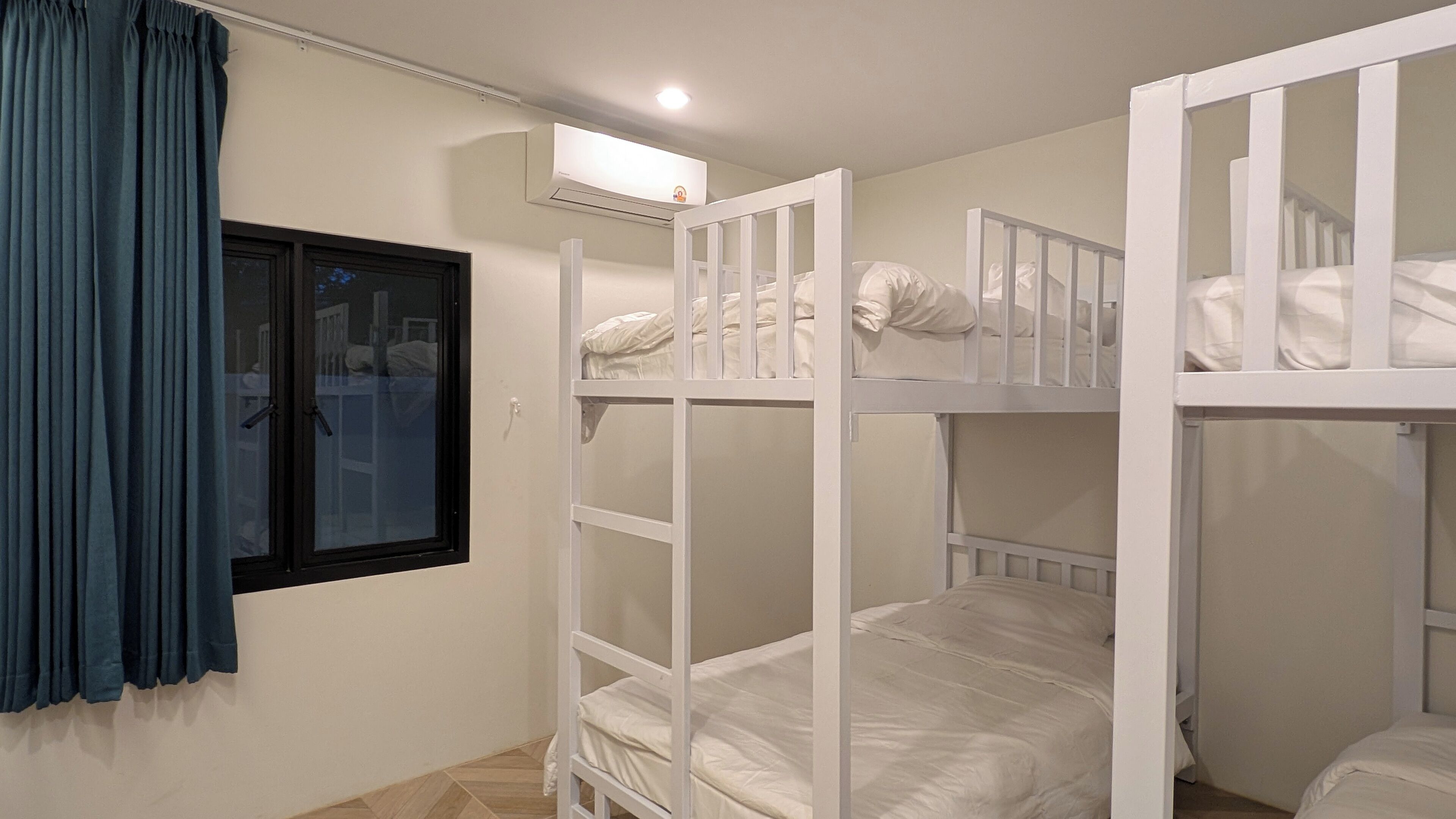 A room with bunk beds, a window with curtains, and a wall-mounted air conditioning unit.