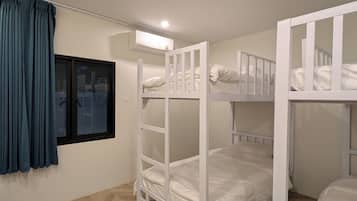 A room with bunk beds, a window with curtains, and a wall-mounted air conditioning unit.