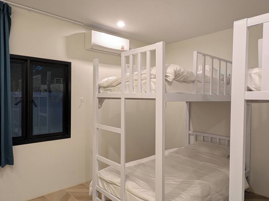 A room with bunk beds, a window with curtains, and a wall-mounted air conditioning unit.