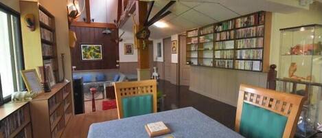 A library with bookshelves, a reading area with chairs, and a table with books.