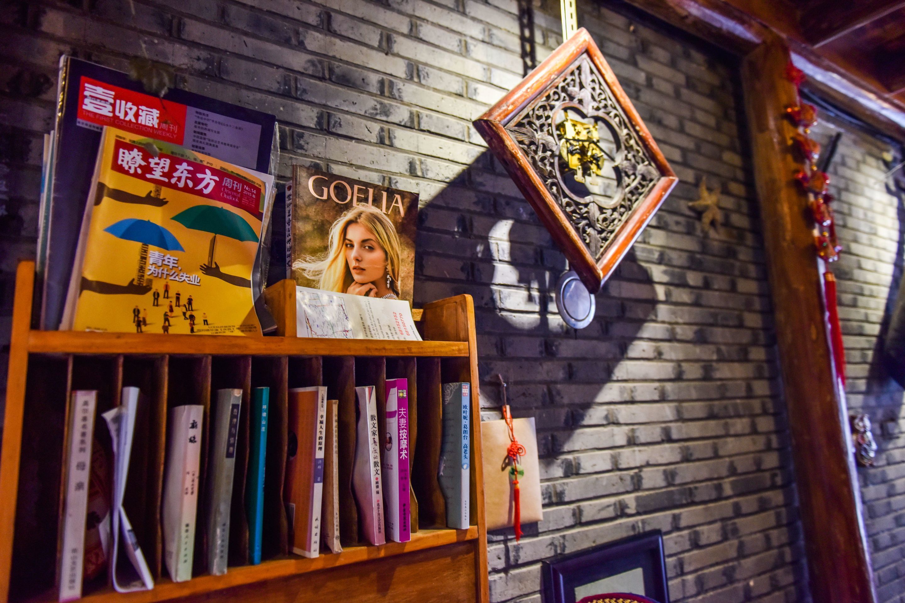 A bookshelf with various books, a framed picture, and a decorative item on a brick wall.