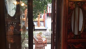 A bathroom with a large, ornate bowl sink, a mirror with decorative carvings, and a window overlooking a courtyard with wicker chairs and a brick wall. - Suzhou Yard (Suzhou)