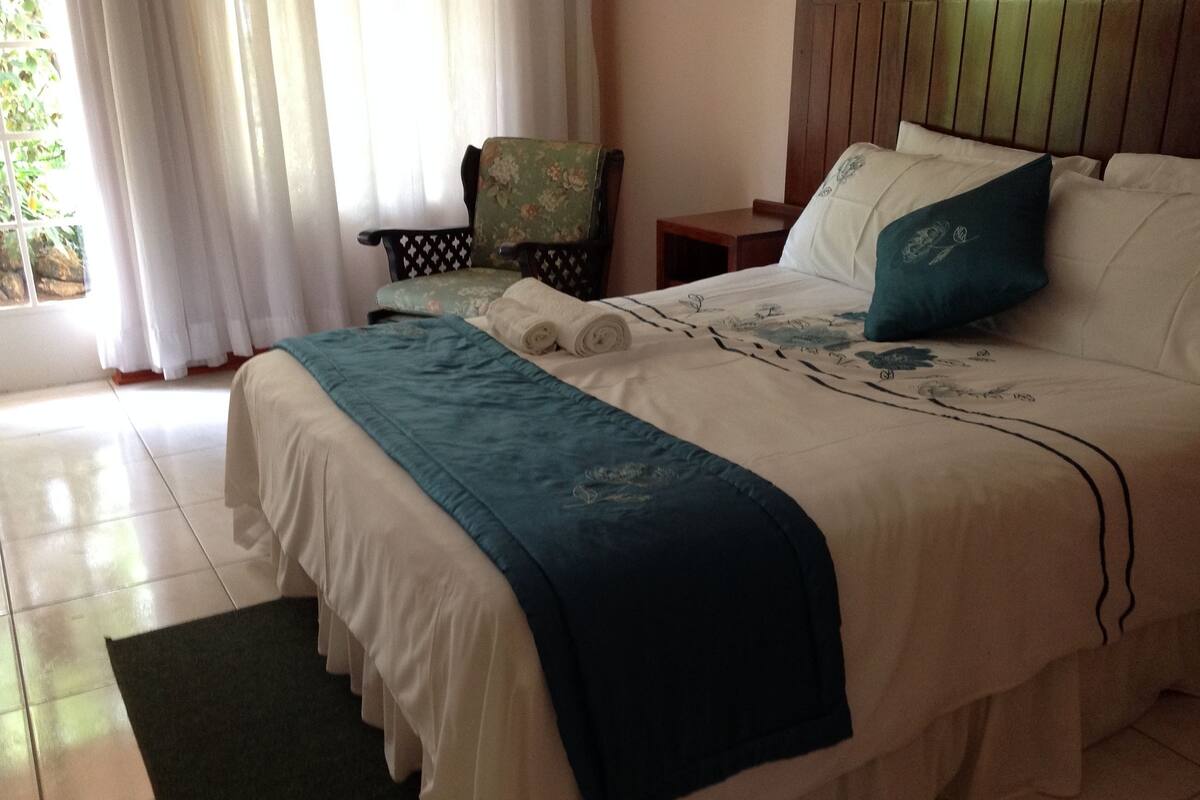 Una cama bien hecha con una colcha azul y blanca, una silla verde y una mesita de noche de madera.