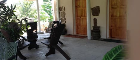 Un espacio al aire libre techado con sillas y mesas, un muro de piedra y puertas de madera.